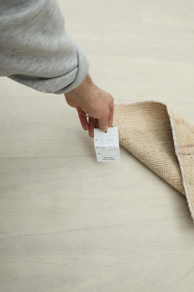 Hand holding a tag near the folded edge of the hand-knotted cream runner, showing its thickness.