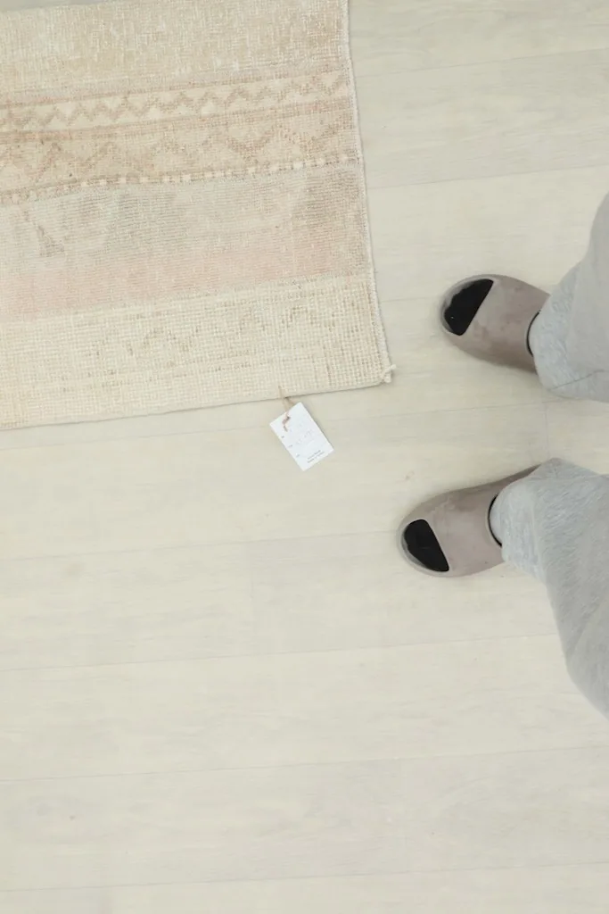 Overhead view of the rug next to feet, providing a sense of scale and showing the product tag.