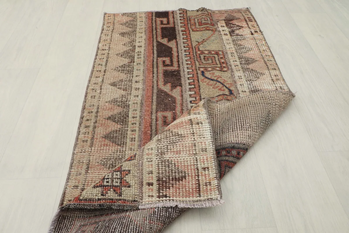 The vintage rug partially folded, showing the thickness of the wool pile and the underlying structure.