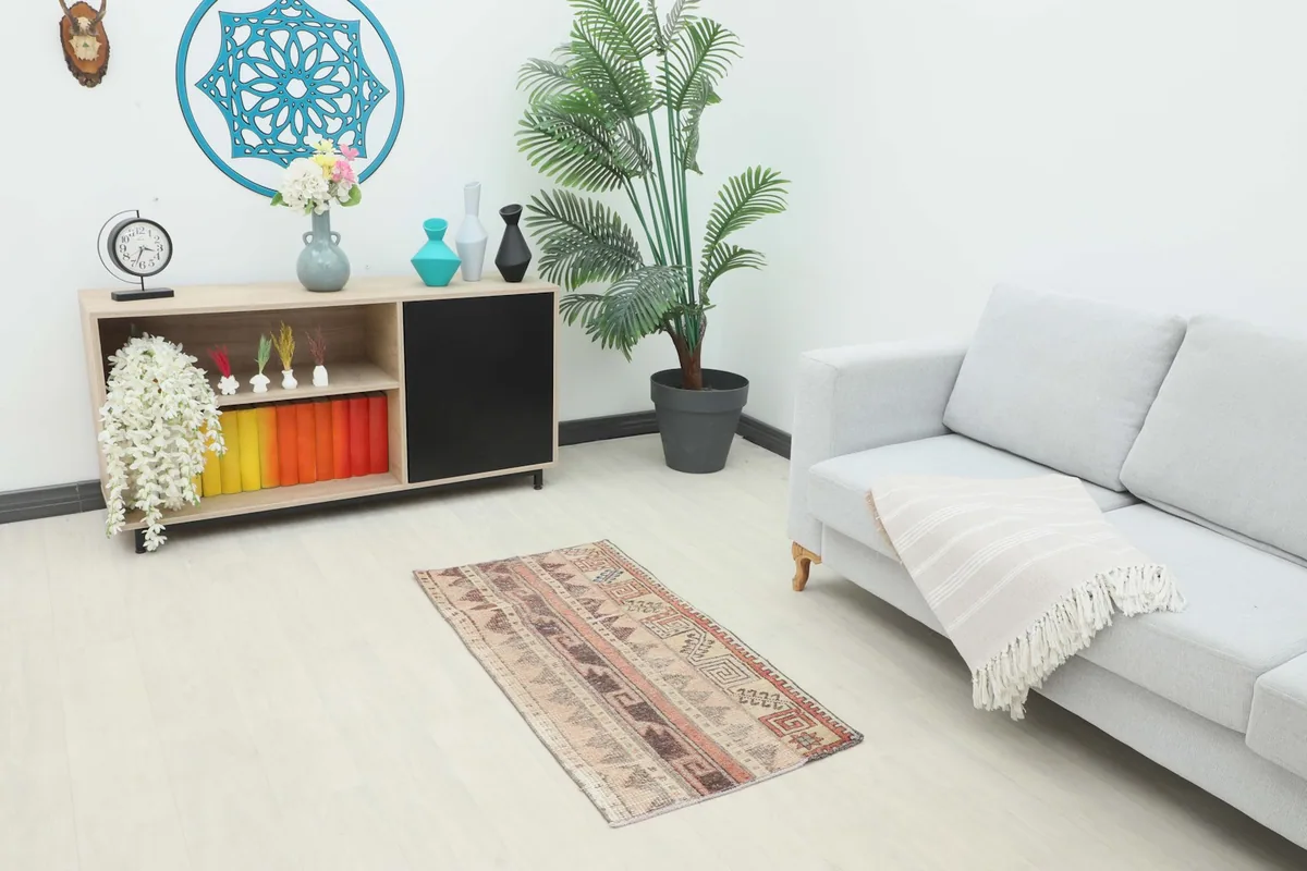 Vintage Anatolian rug displayed in a living room setting next to a sofa and cabinet, showing its scale.