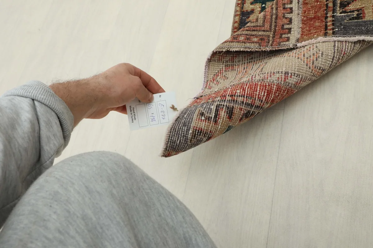 A hand holding a tag near the folded rug, indicating its size and authenticity