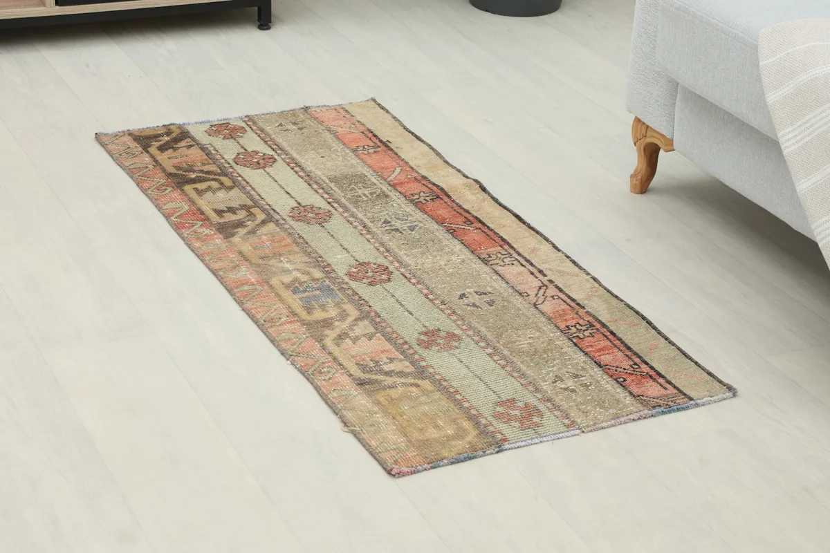 Angled view of the rust and beige patchwork rug on a light floor, showing its full length