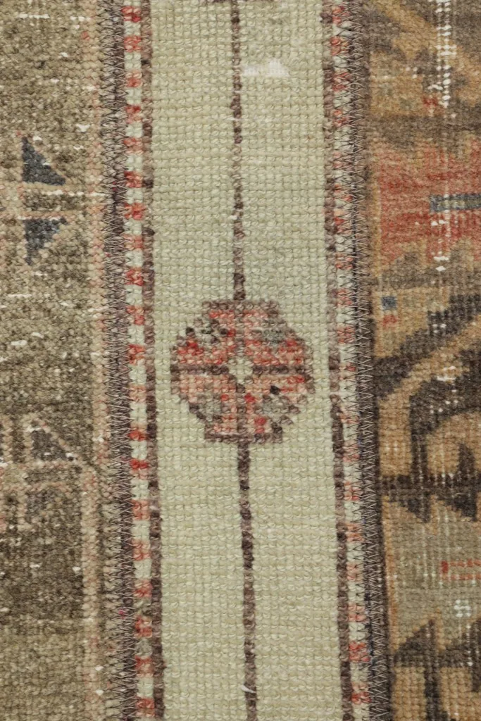 Vertical close-up of a central olive and rust patterned strip within the patchwork rug