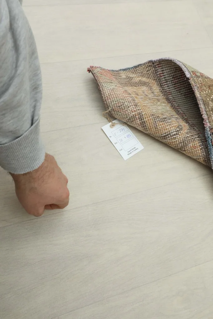 Hand holding the rug with its tag, showing the thickness and material details