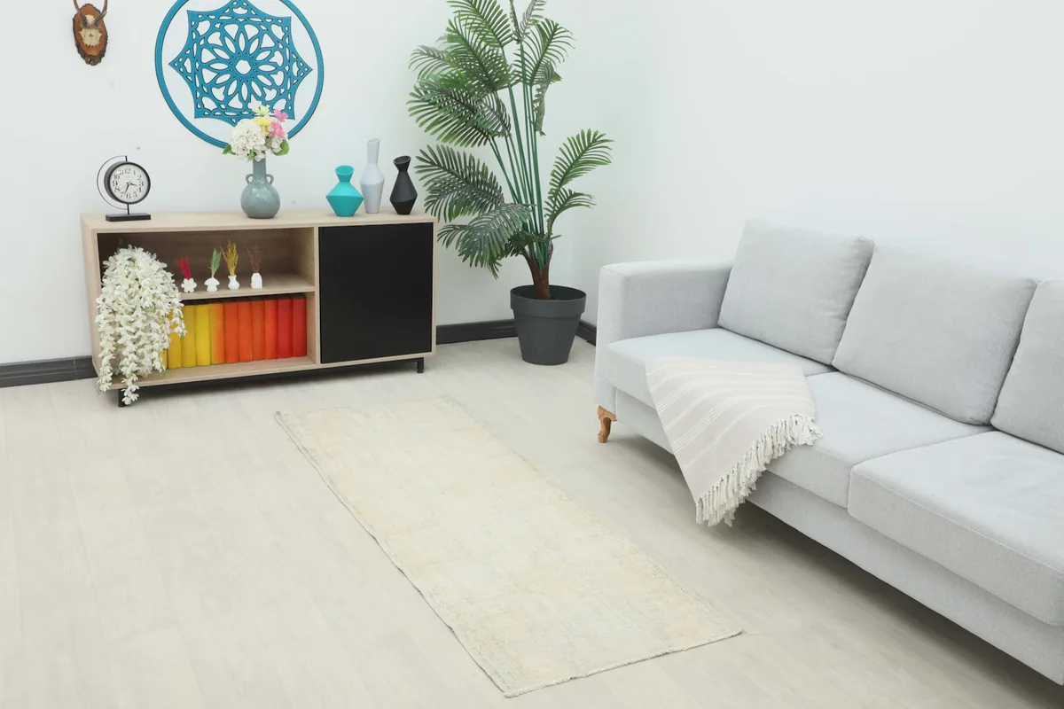 Ivory runner rug placed in a modern living room setting with a light gray sofa and wooden cabinet.
