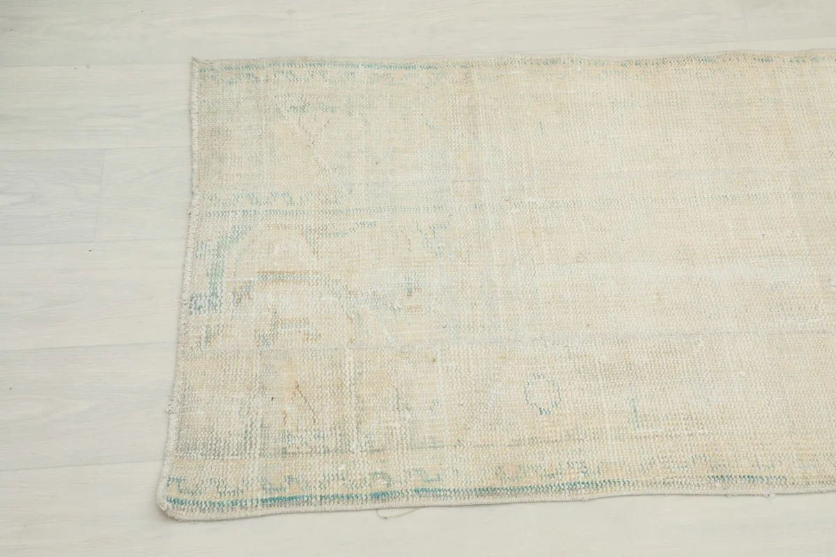 Detailed view of the rug's edge and part of the main field, revealing its faded design and texture.
