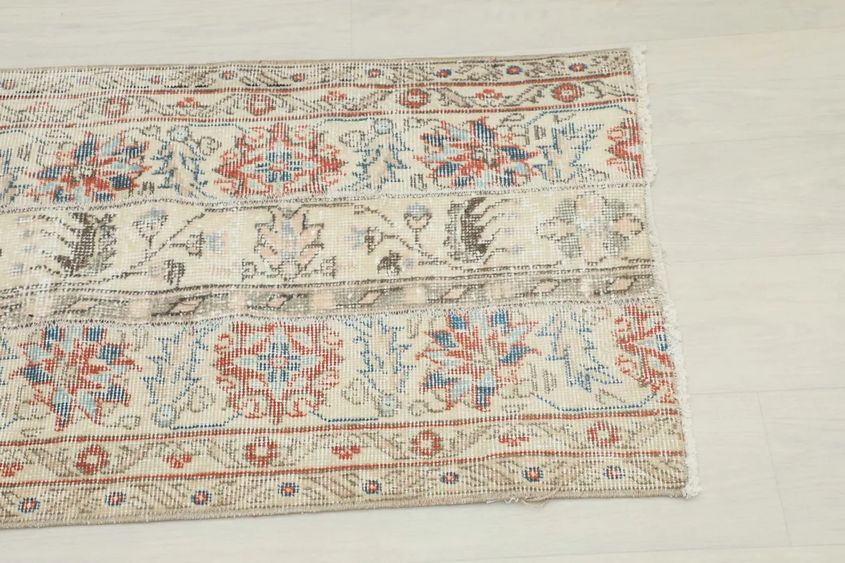 Close-up view of the rug's floral and geometric patterns in beige, red, and blue tones.
