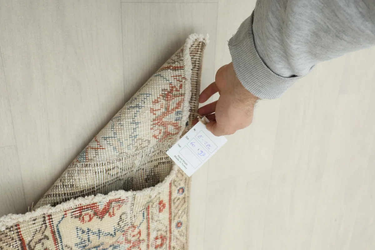 Hand holding a label near the back of the rug, showing the dense knotting on the foundation.