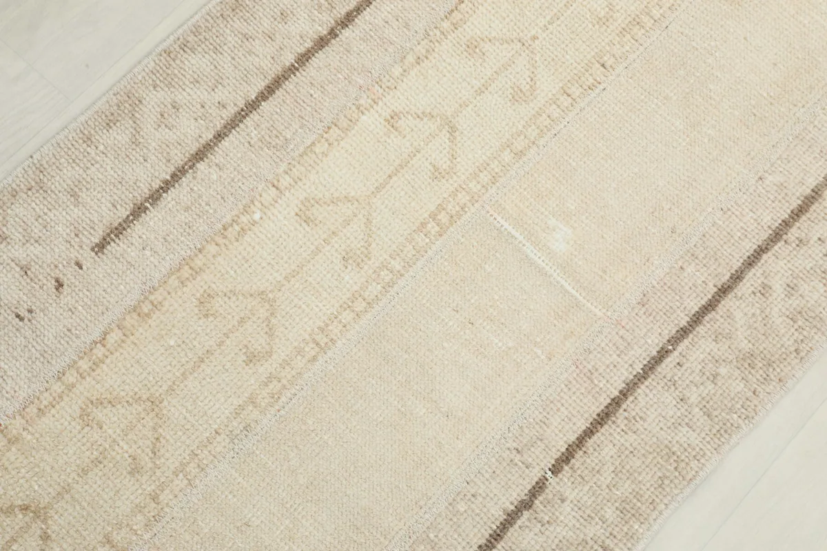Overhead detail of the rug's center, focusing on the repeating geometric motifs in beige and tan.