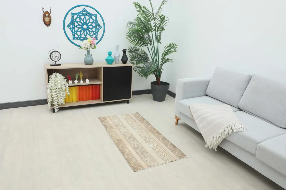 Vintage beige and tan rug placed in a modern living room setting with a light gray sofa and wooden cabinet.