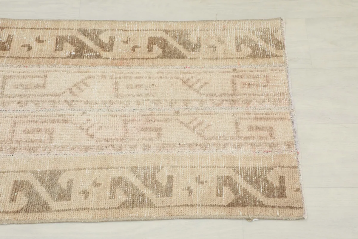 Close-up of the rug's end, highlighting the brown tribal patterns and tan field.