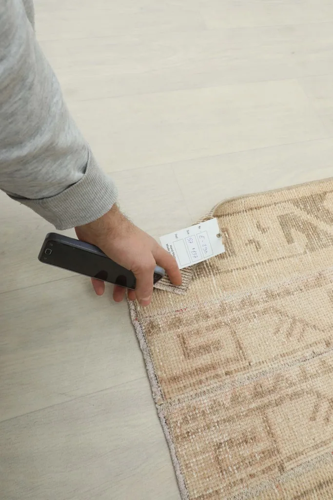 Hand holding a tag near the rug's edge, indicating quality and authenticity.