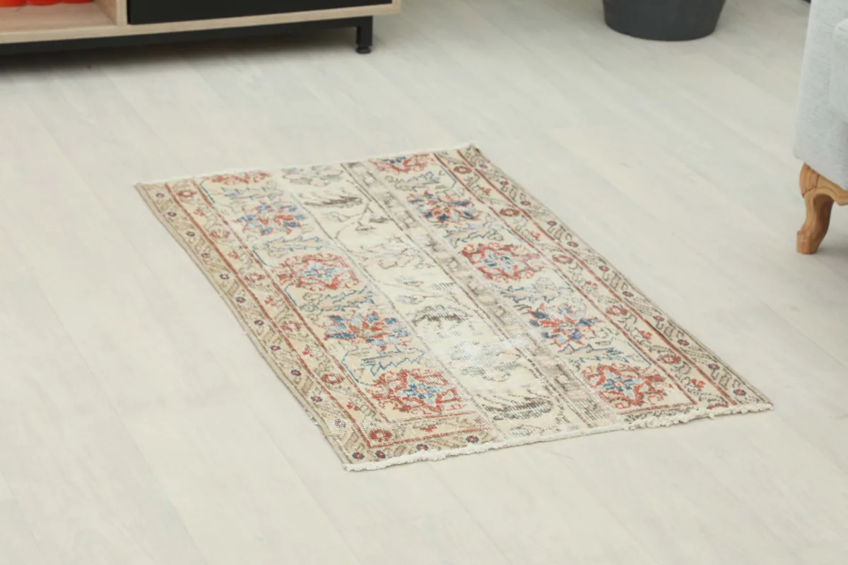 Angled view of the beige vintage rug on a light floor, showing its full pattern