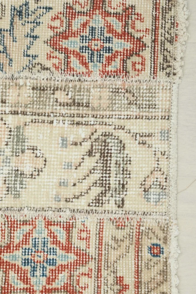 Extreme close-up of the rug's edge, showing red and blue motifs and the fringe