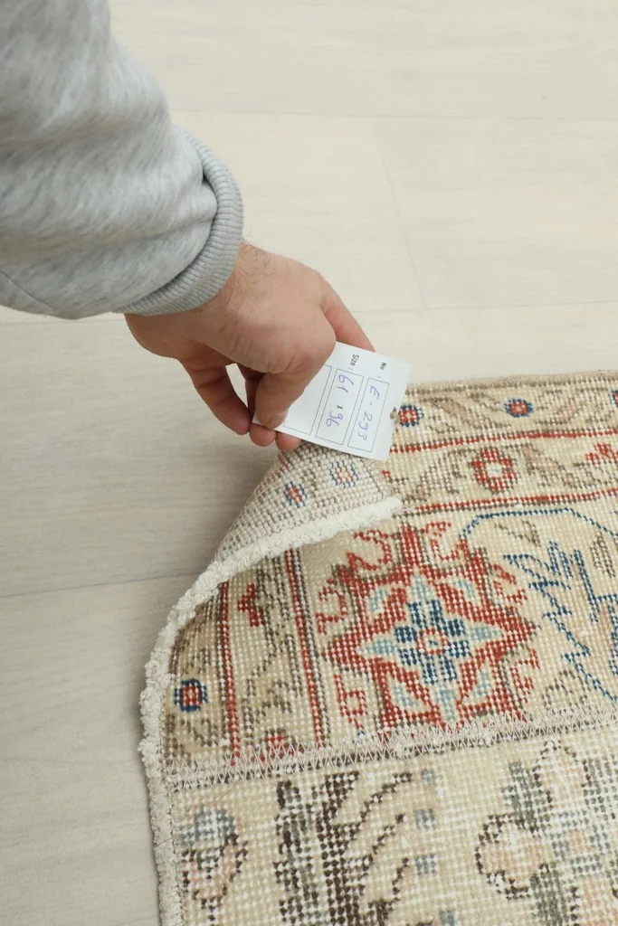 Hand holding a tag on the rug's corner, showing the details of the vintage Anatolian piece