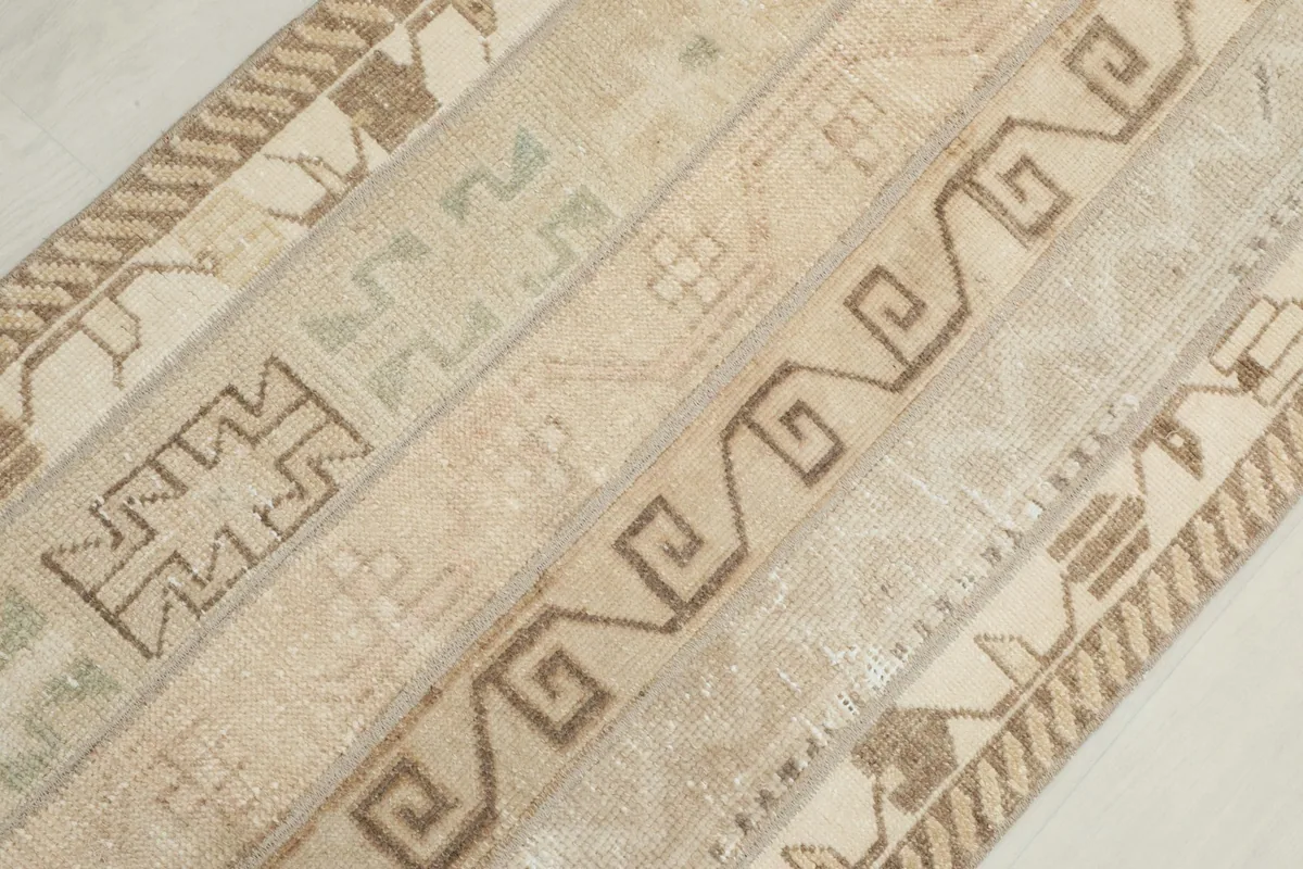 Diagonal close-up view of the rug's surface, revealing the intricate geometric designs and subtle olive tones.