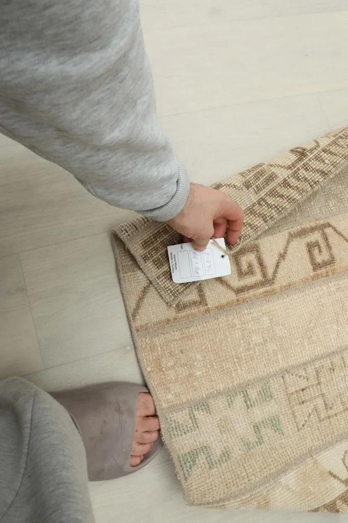 Hand holding a tag near the rug, illustrating the rug's size and quality.