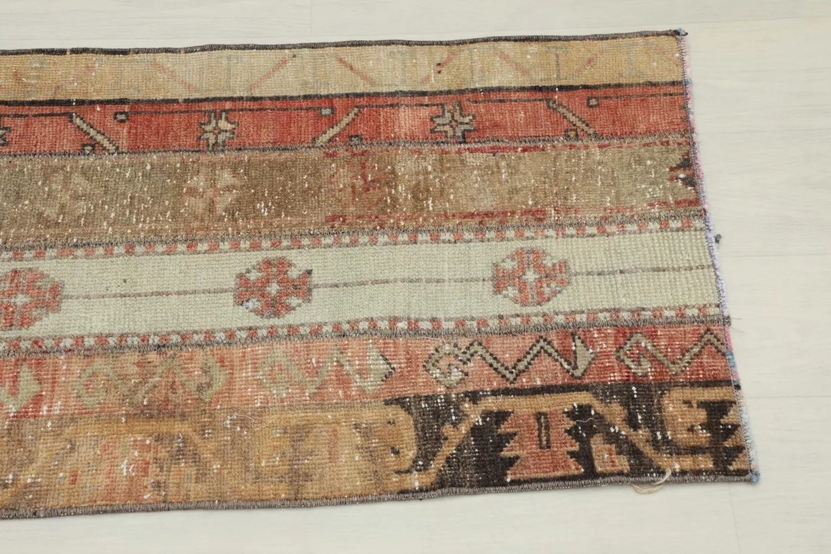 Close-up detail of one end of the rug, showing the geometric patterns and color variations in beige, rust, and brown.