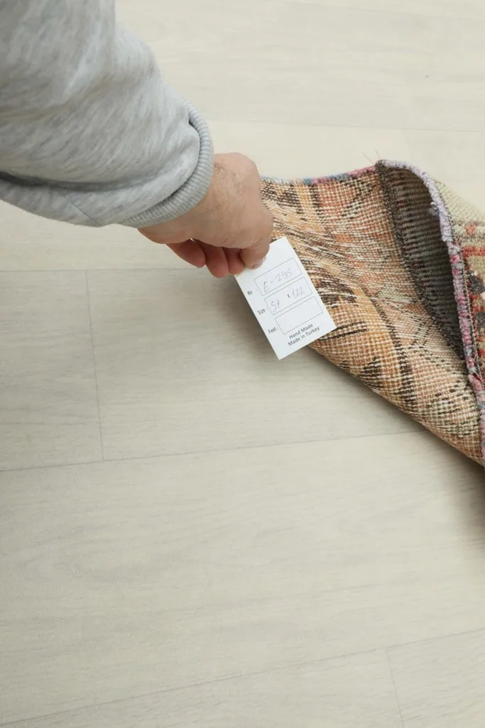 Hand holding a tag near the folded rug, indicating its authenticity and professional cleaning.