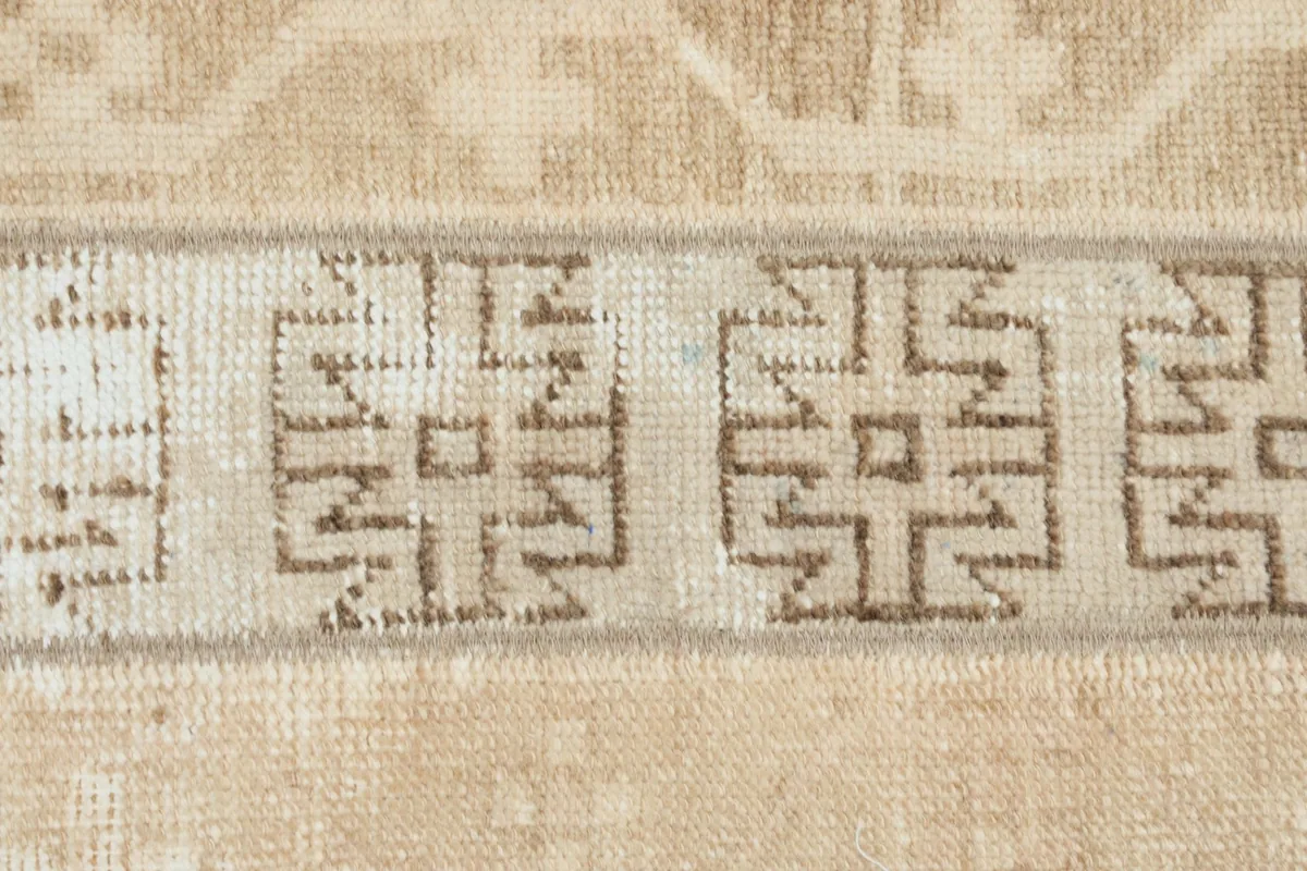 Detailed view of the brown geometric motifs against the beige background, showing the wool pile texture.