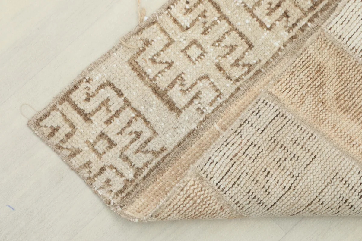 Corner of the rug folded over, showing the cotton foundation and the reverse side of the hand-knotted pile.