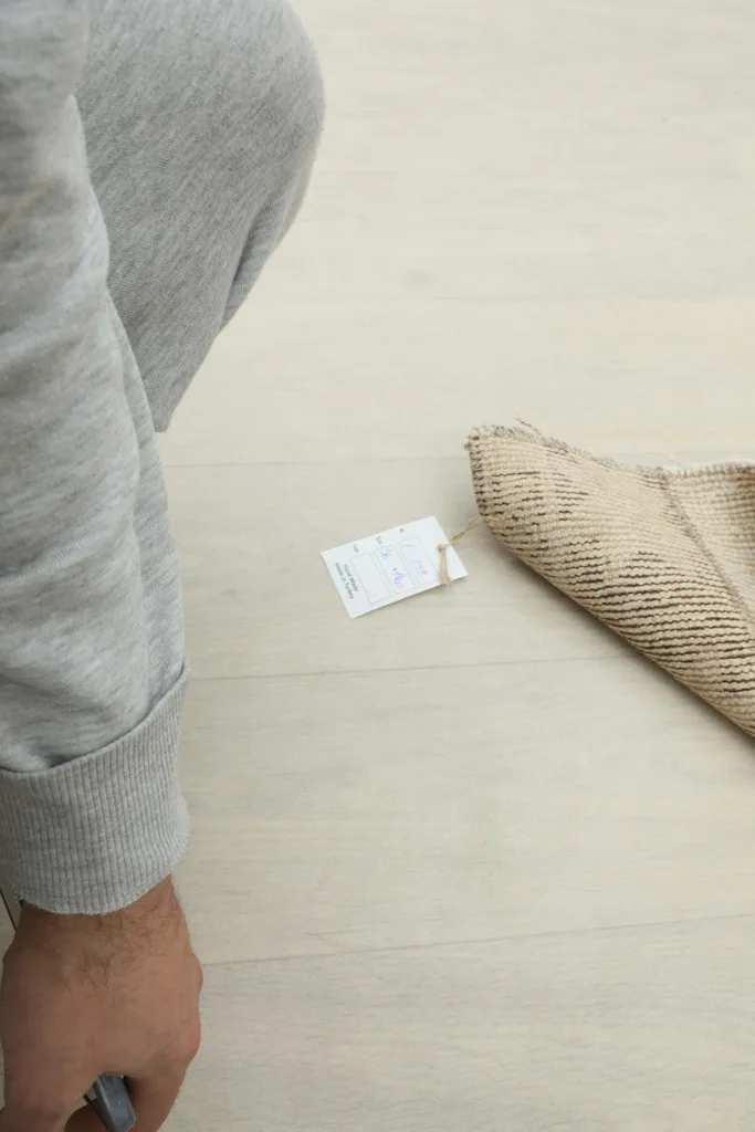 A person's hand next to the rolled rug and a tag, indicating the rug is prepared for shipment.