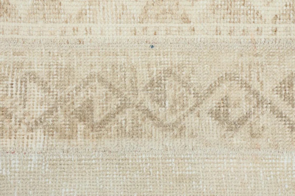 Extreme close-up on the hand-knotted wool pile and the subtle color variations in the beige and tan.