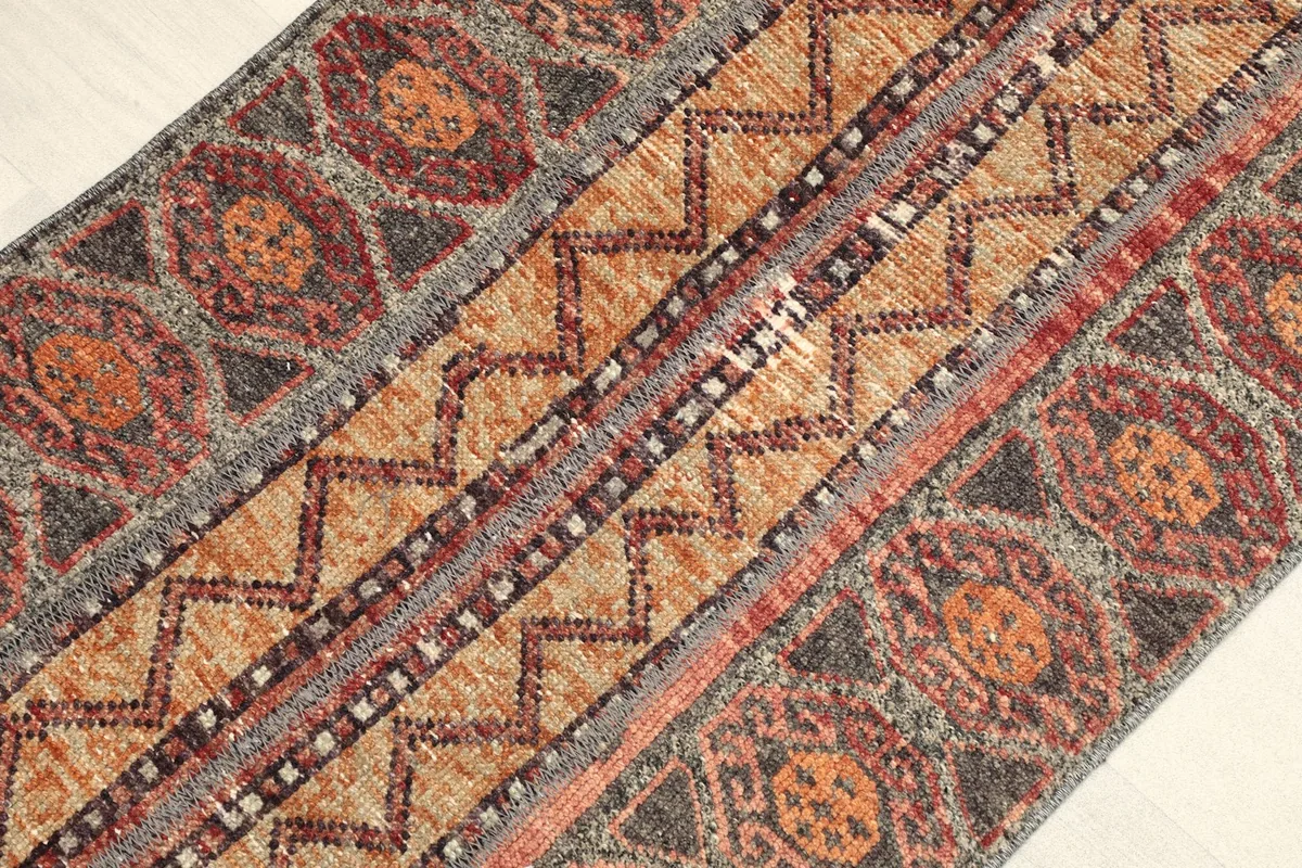 Angled view of the rug's surface, revealing the varied orange, red, and gray geometric designs.