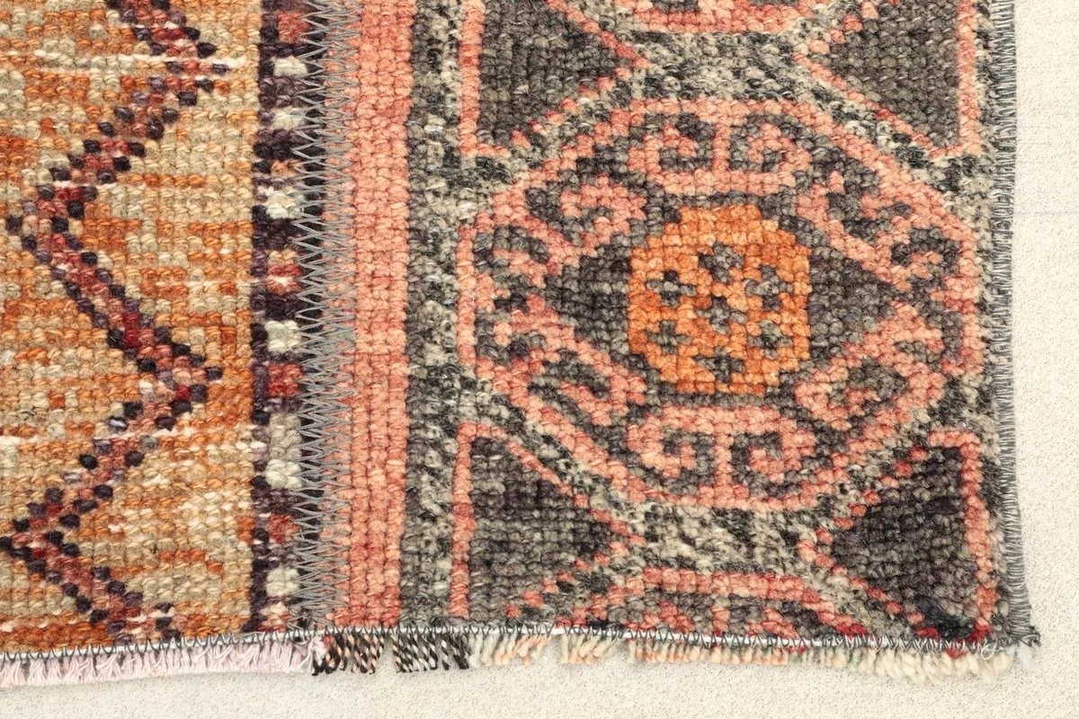Close-up detail of the rug's end, showing pink, gray, and orange geometric motifs and fringe.