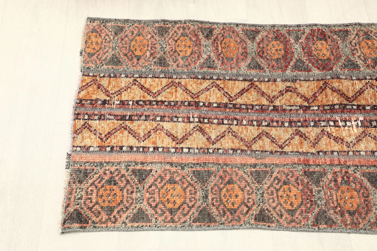 Overhead view of one half of the rug, showing the progression of orange, gray, and red geometric designs.