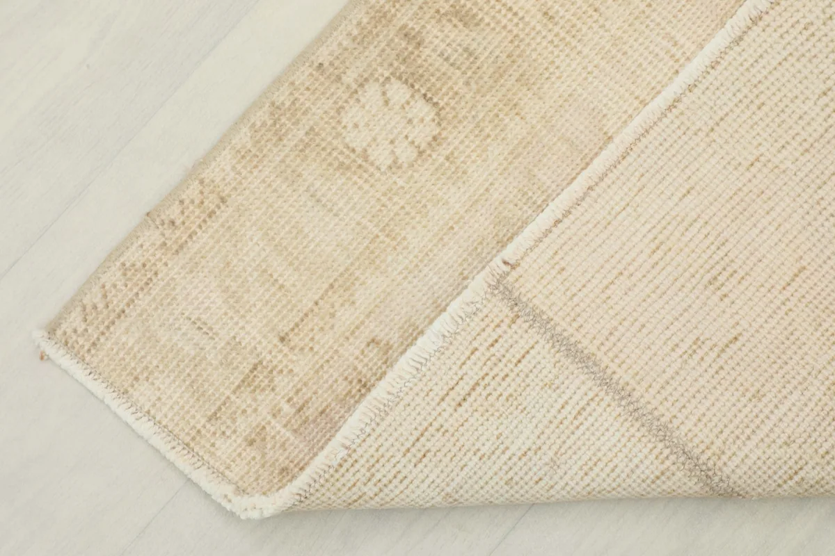 Corner of the rug folded back, displaying the wool pile on the front and cotton foundation on the back.