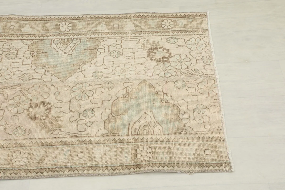 Close-up detail of the rug's border and floral patterns in beige, tan, and green.