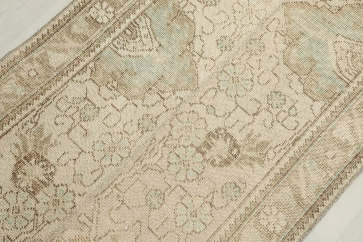 Detailed view of the rug's surface, showing the subtle green and tan motifs against the beige field.
