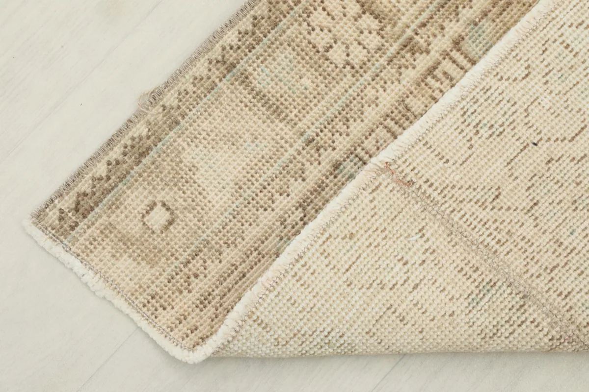 View of the back of the rug, showing the cotton foundation and knotting detail, with a corner folded.
