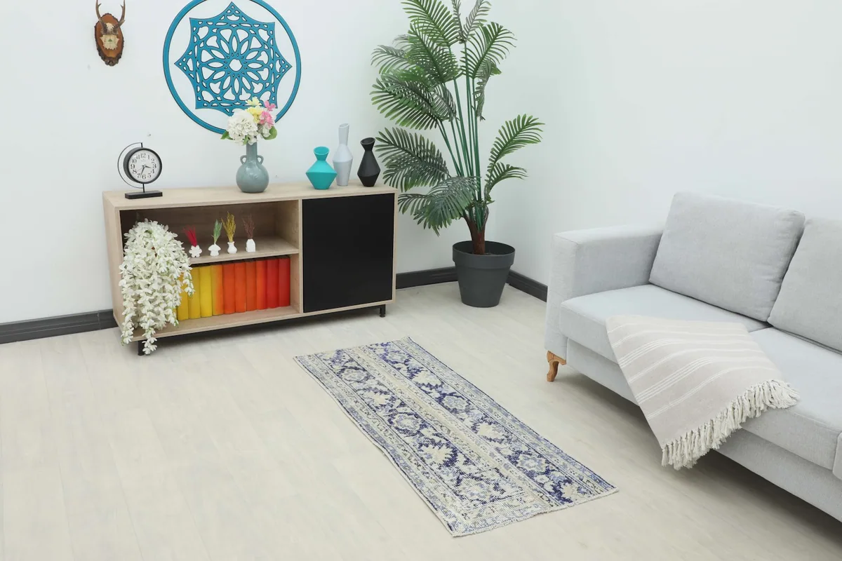 Vintage blue and ivory runner rug placed in a modern living room setting next to a sofa and console table.