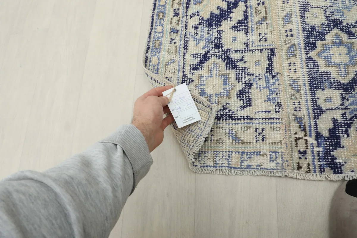 A hand holding the product tag, indicating the rug's authenticity and care instructions.