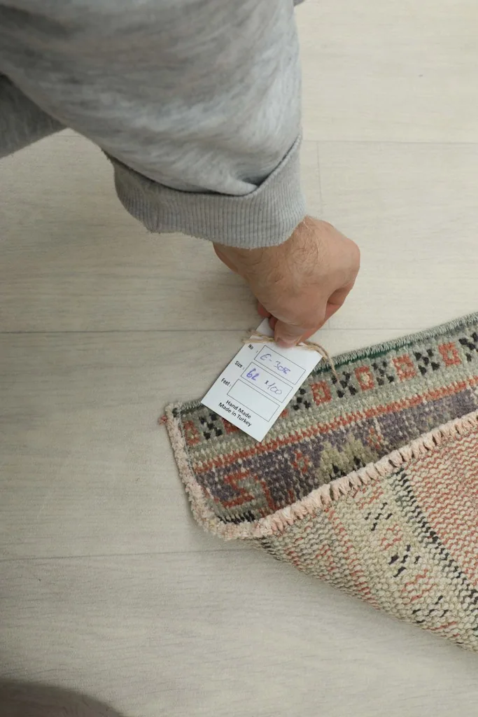 Hand holding a tag near the rug, indicating its authenticity and origin