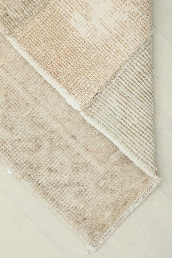 View of the rug's reverse side and folded corner, showing the hand-knotted cotton foundation.