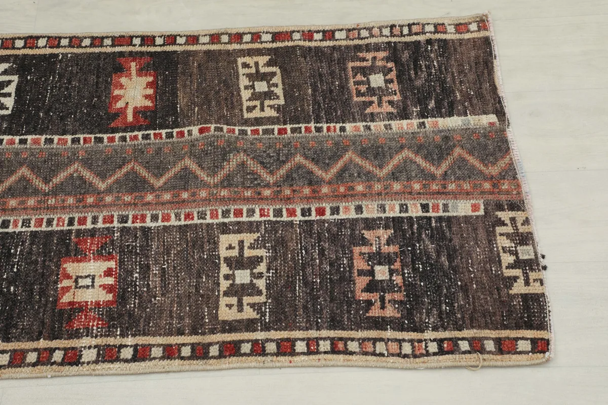 Close-up detail of the rug's end, showing brown, red, and beige geometric patterns and texture.