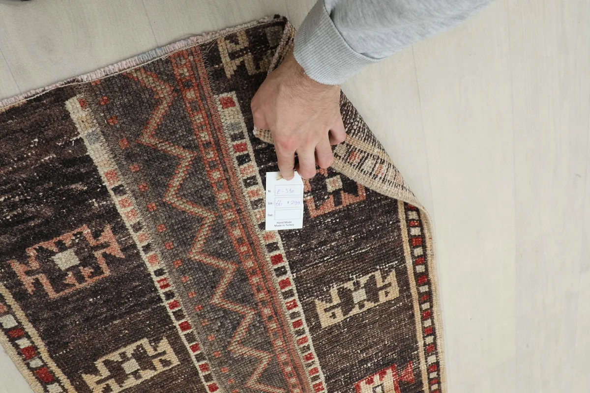 Hand lifting a corner of the rug to show the back of the hand-knotted wool and cotton foundation.