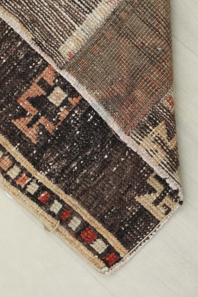 Corner of the rug folded back, revealing the underside and the hand-knotted construction.