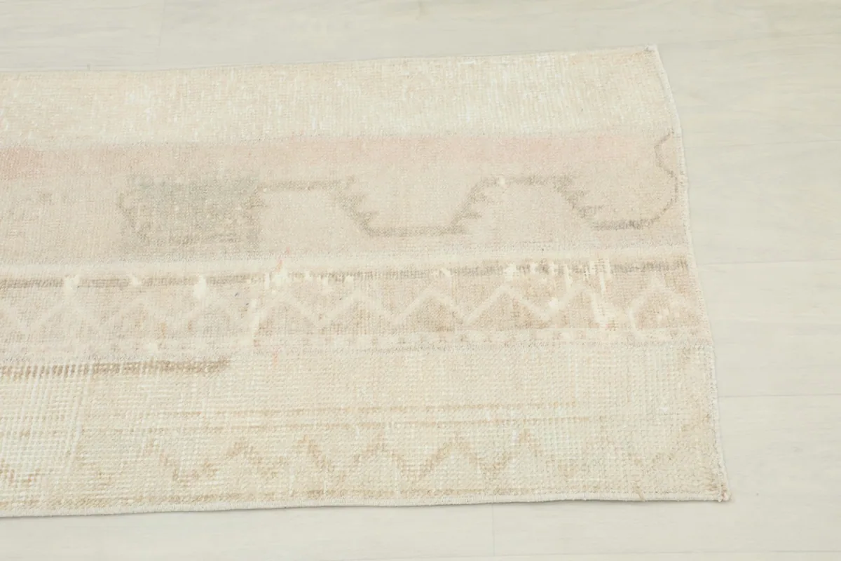 Close-up detail of the rug's beige and tan geometric patterns with hints of rose and gray