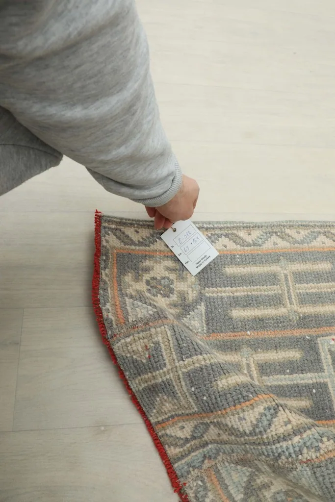 Hand holding a tag near the rug's edge, showing the texture and colors up close
