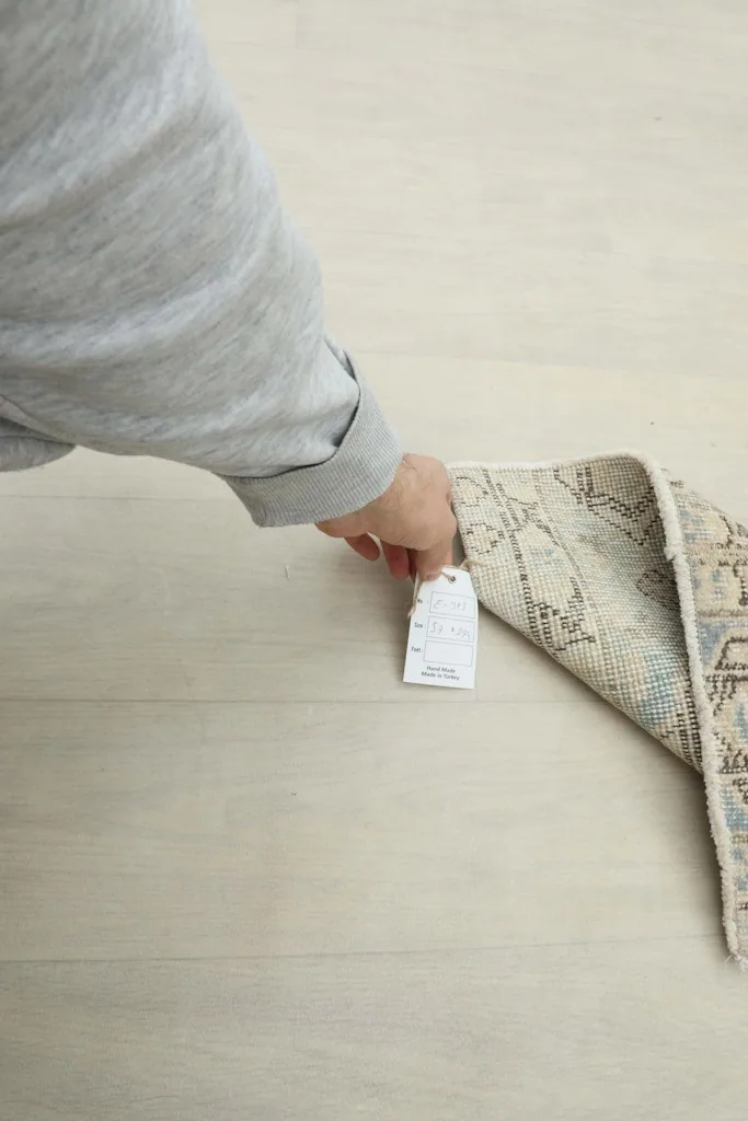 Hand holding a tag near the edge of the blue and beige vintage Anatolian runner.
