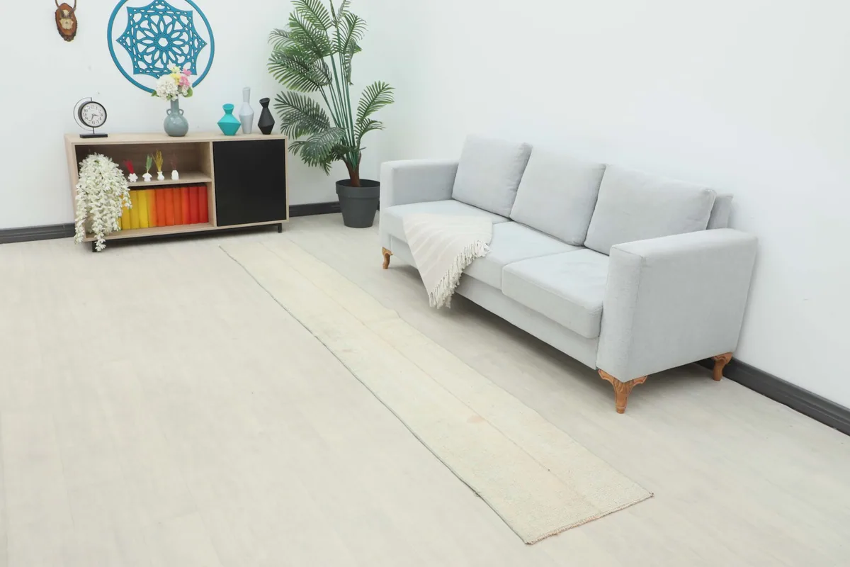 Long view of the cream runner rug in a room setting next to a light gray sofa.