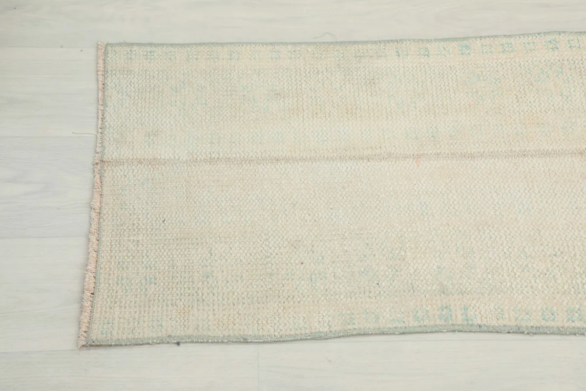 Detail view of the other end of the cream runner rug, highlighting its texture and faded appearance.