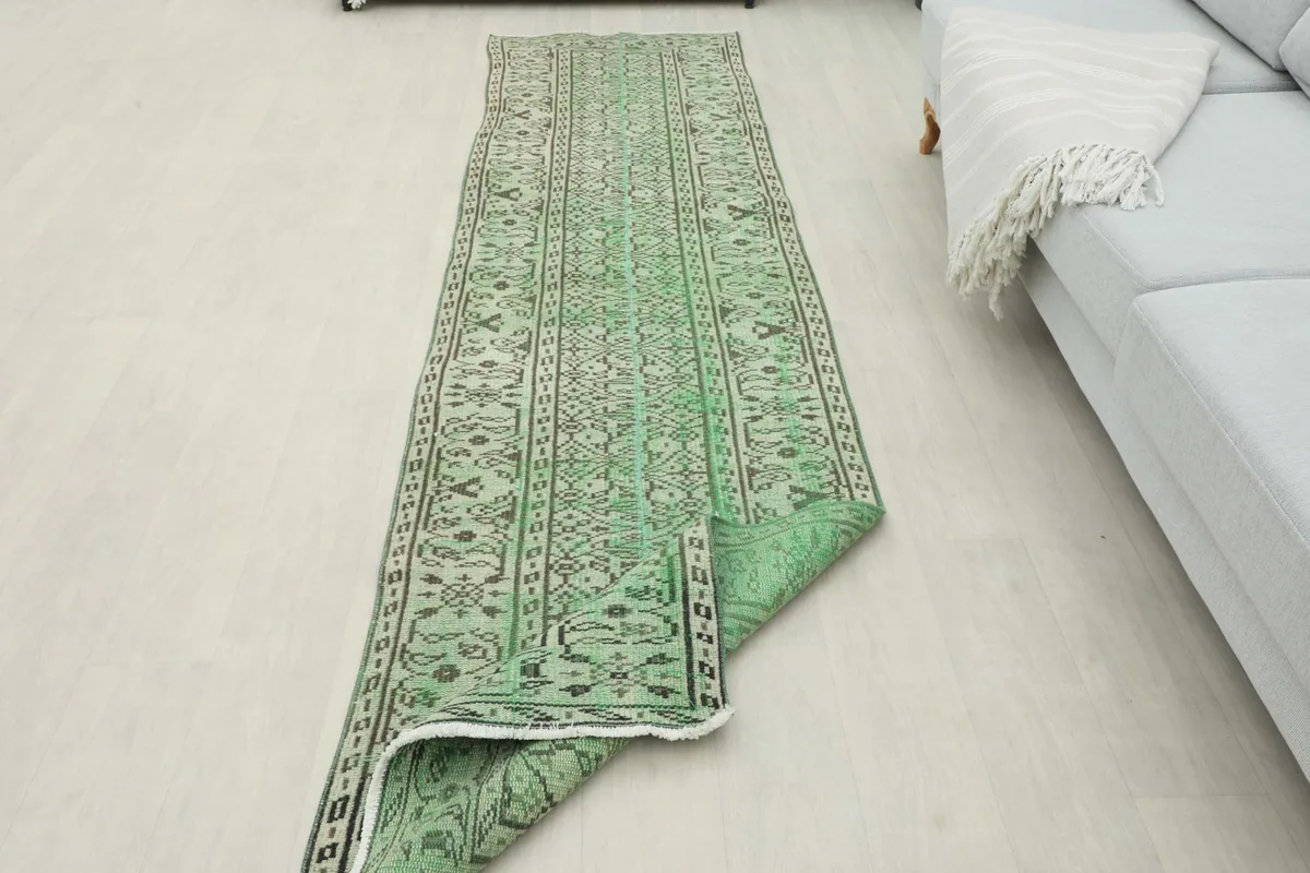 Angled view of the green runner rug partially rolled, showcasing its flexibility