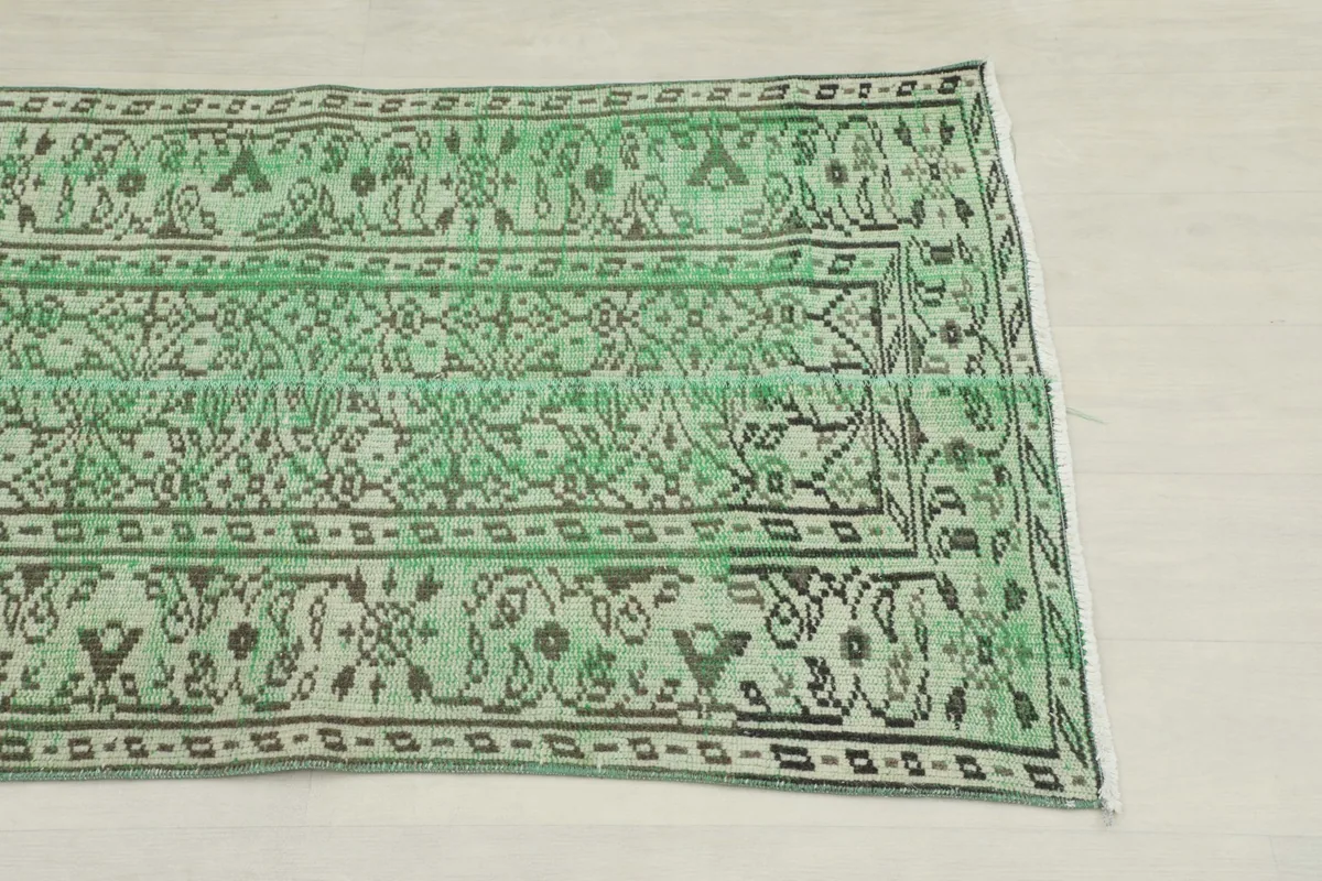 Close-up detail of the green rug's geometric and floral patterns with black and cream accents