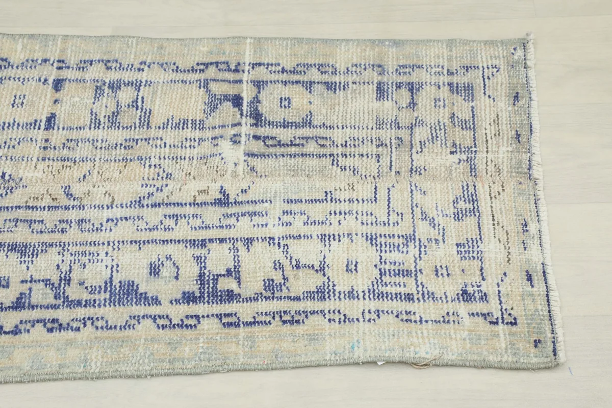 Close-up detail of the rug's end, showing the faded blue geometric patterns on a beige field.