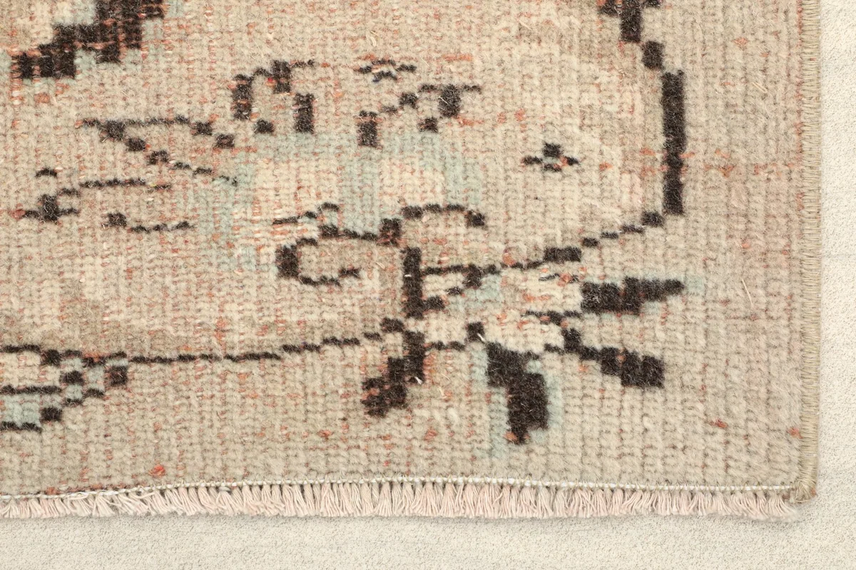 Close-up detail of the rug's border showing faded green and orange accents in the brown motifs.